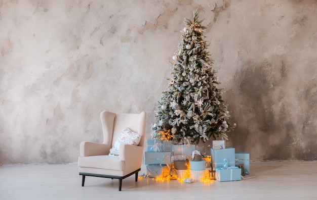 Arbre décoré de Noël avec des cadeaux et une chaise sur le fond du mur dans le salon.