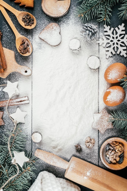 Arbre de Noël, biscuits au pain d'épice, accessoires de cuisson et ingrédients sur table noire avec de la farine. Espace de copie. Verticale