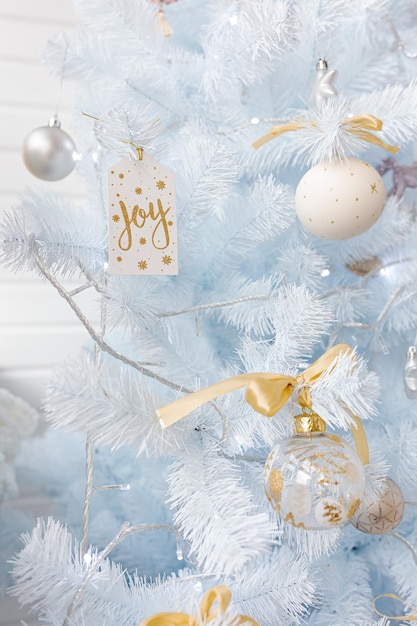 Arbre de Noël blanc décoré de boules de Noël rose doré argenté et de belles boules de verre et signe Joy sur une branche bleue blanche étincelante et féerique, lumières décoratives, espace de copie. photo