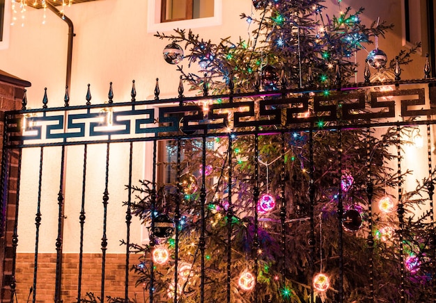 L'arbre de Noël brille dans la cour de la maison derrière la clôture la nuit