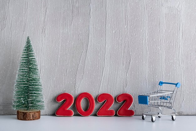 Arbre de Noël, chariot et numéros 2022 sur fond clair. Shopping pour la nouvelle année. Espace de copie