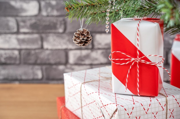 Arbre de Noël décoré avec de beaux cadeaux rouges et blancs emballés à la maison avec un concept de design festif de mur de briques noires en gros plan