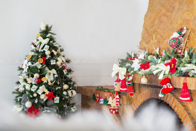 Arbre de Noël décoré et cheminée en pierre avec guirlande et branches d'arbre de Noël jouets arcs bottes tricotées boules fleurs de poinsettia