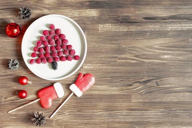 Arbre de Noël drôle en forme de baies de framboises fraîches sucrées sur plaque sur fond de bois pour le petit-déjeuner des enfants. nourriture de noël avec des décorations du nouvel an avec espace de copie