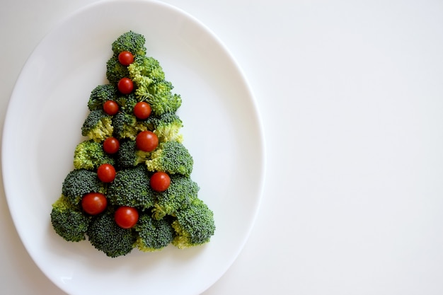 Arbre de Noël fait de brocoli et de petites tomates sur plaque blanche sur fond blanc. Aliments biologiques sains.