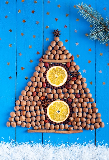 Arbre de Noël fait de noix et de fruits secs sur le fond en bois avec des étoiles, de la neige et une branche de sapin