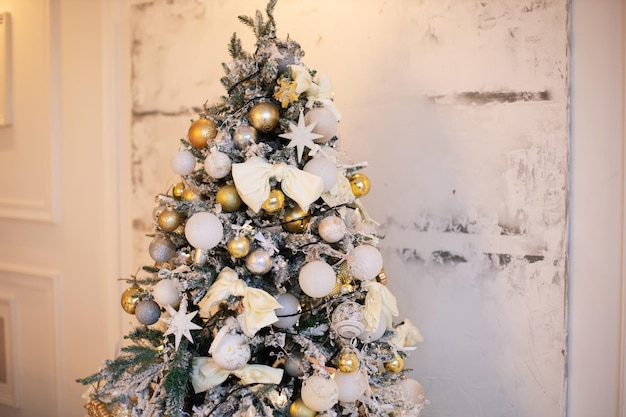 L'arbre de Noël de neige se tient à la maison contre le mur blanc avec des jouets de ballon d'or