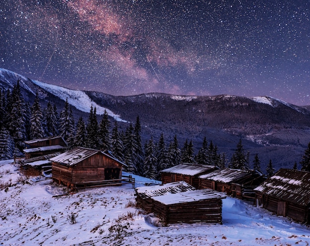 arbres d'hiver enneigés magiques et village de montagne. Ciel nocturne vibrant avec des étoiles et une nébuleuse et une galaxie.