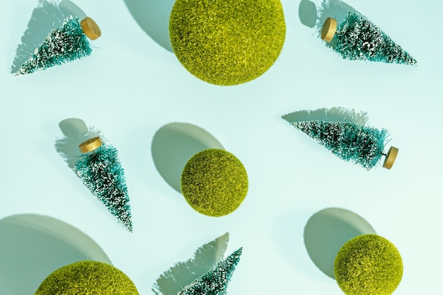 Arbres de Noël jouets et boules d'herbe verte éparpillées sur fond bleu. Modèle conceptuel avec des ombres dures