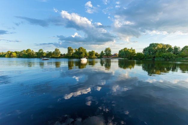 Les arbres verts se reflètent dans l'eau de la rivière. Dans le ciel, il y a des nuages dramatiques.