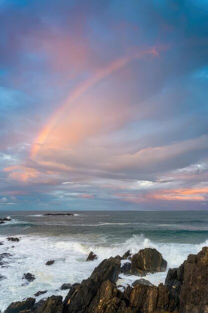 Un arc-en-ciel apparaît au-dessus de l'océan au coucher du soleil.