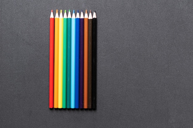 Un arc-en-ciel de crayons de couleur et de marqueurs sur fond sombre