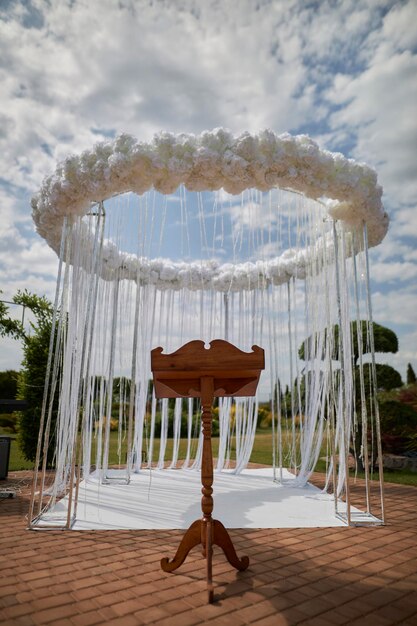 arc de mariage des jeunes mariés et un support en bois pour le prêtre fils et fleurs blancs étincelants