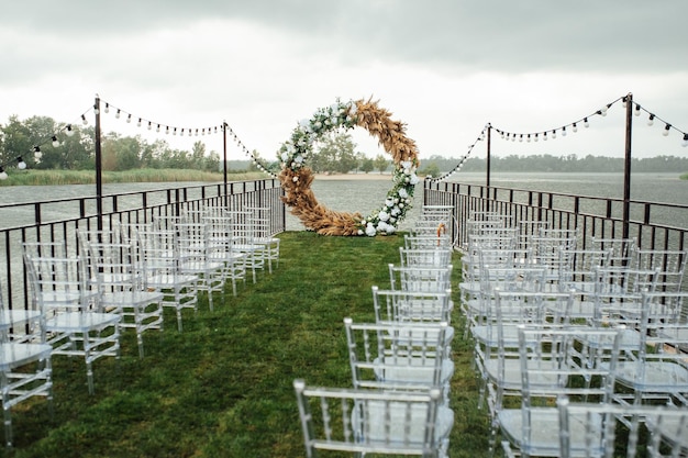 Arc en plein cintre pour une cérémonie de mariage au bord de la rivière. Des chaises en verre blanc se tiennent pour les invités