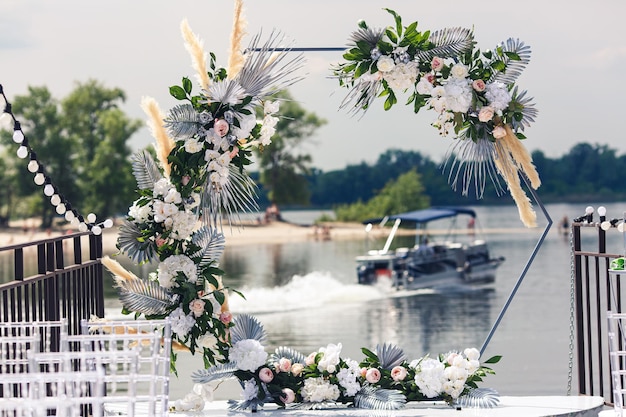 Arche hexagonale de mariage décorée de belles fleurs sur la jetée du bateau sur la rivière en arrière-plan