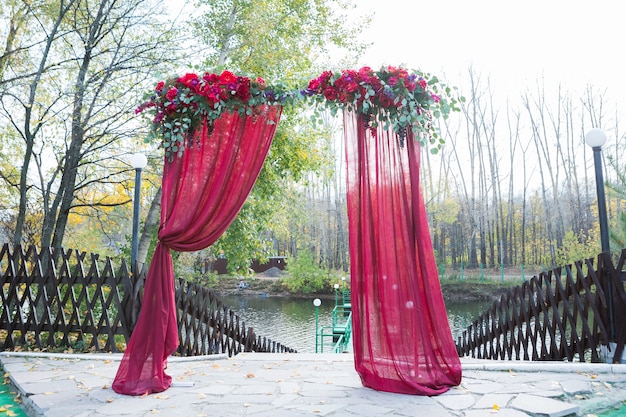 L'arche pour la cérémonie de mariage, décorée de fleurs en tissu et de verdure, se trouve dans une forêt de pins