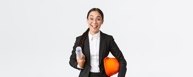 Architecte asiatique excitée et talentueuse commençant à travailler sur la construction tenant des plans et un casque de sécurité portant un costume d'affaires rencontrant des ingénieurs dans la zone de construction souriant fond blanc heureux