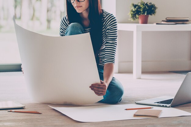 Architecte confiant. Gros plan sur une belle jeune femme confiante examinant le plan alors qu'elle était assise par terre à la maison