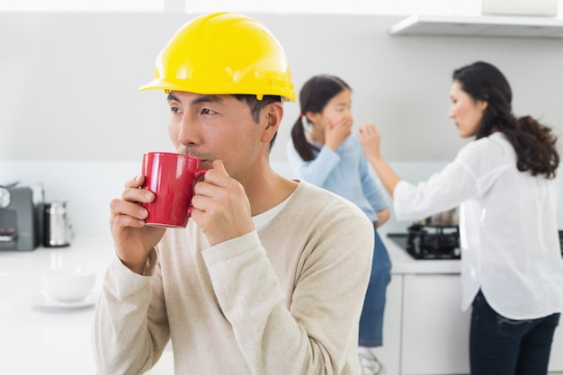 Architecte dans un casque, boire du café avec la famille en arrière-plan