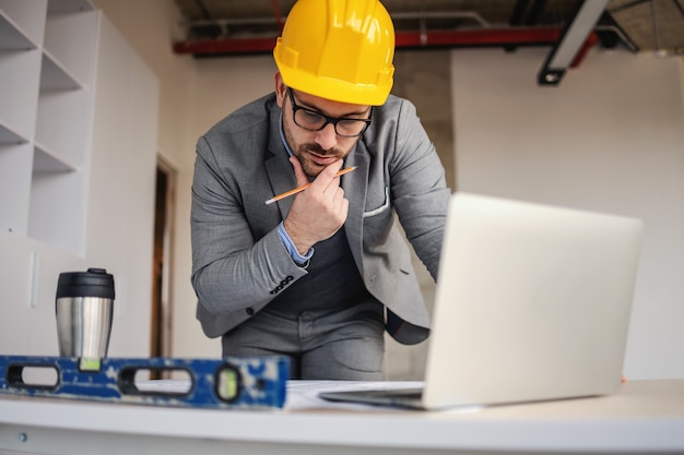 Architecte focalisé regardant les plans et la réflexion tout en s'appuyant sur le bureau sur le chantier de construction.