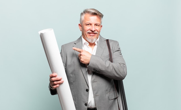 Architecte principal souriant joyeusement, se sentant heureux et pointant vers le côté et vers le haut, montrant l'objet dans l'espace de copie