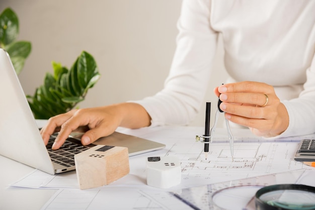 Architecte tapant un clavier d'ordinateur portable pour examiner la conception de la maison avant de l'éditer avec une boussole