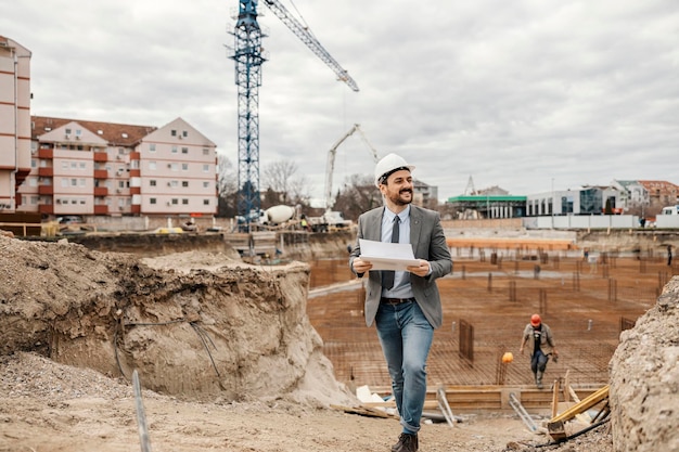 Un architecte tient des papiers et visite le chantier de construction