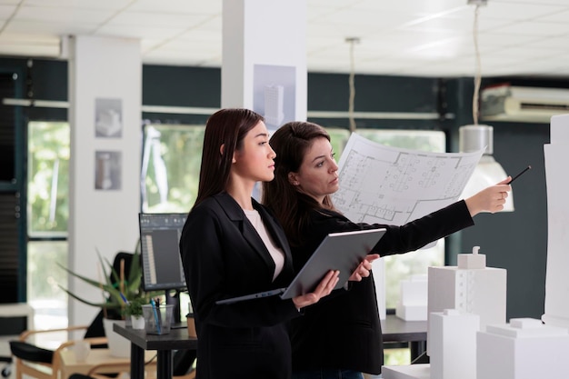 Architectes détenant un plan directeur, travaillant avec un projet de construction de bâtiments dans un bureau d'architecture, modélisant une maison en 3d, utilisant un logiciel sur un ordinateur portable. Ingénierie des concepteurs, travailleurs de l'immobilier