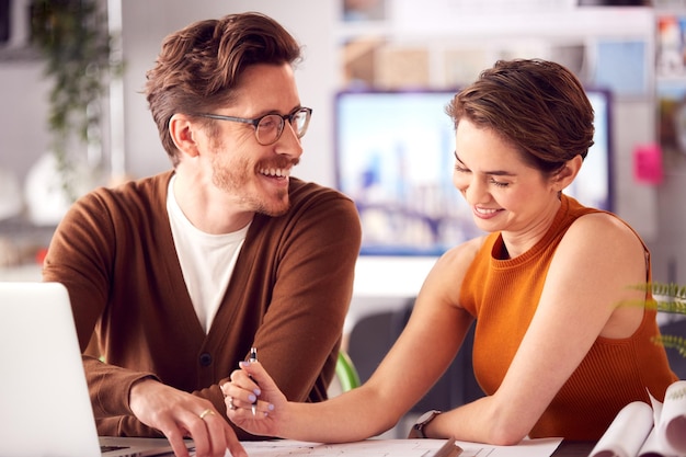 Architectes masculins et féminins au bureau travaillant au bureau sur un ordinateur portable et regardant des plans