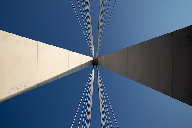 Architecture abstraite minimaliste tournée avec un pilier en béton blanc d'un pont suspendu avec deux faisceaux de câbles de suspension contre un ciel bleu clair