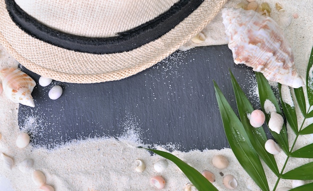 Ardoise noire vide sur le sable avec chapeau et coquillages