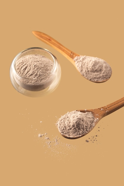 Argile sèche pour masque facial dans un bol en verre et cuillères en bois sur fond beige neutre Concept de soins personnels