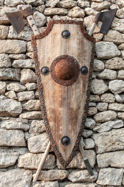 Armes anciennes sur un mur de pierre. Bouclier en bois avec des accents et des haches en fer.