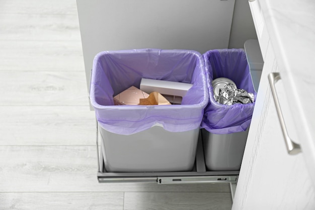 Armoire ouverte avec poubelles pleines pour une collecte séparée des déchets dans la cuisine