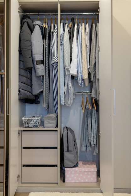 Armoire avec des vêtements d'ordre parfait dans des tons bleus et clairs sur les cintres et des objets dans des conteneurs