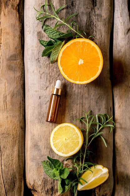 Photo arôme de citron et d'orange à la menthe essentielle de romarin bio ou huile cosmétique à partir d'ingrédients frais dans une bouteille en verre avec pipette concept promotionnel pour les soins du corps de la peau effet antistress fond en bois