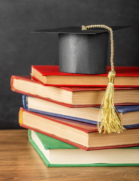 Photo arrangement de différents livres avec un chapeau de graduation