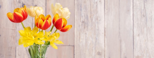 Arrangement de fleurs de tulipes dans un vase en verre avec un décor d'arrosoir de souhaits de coeur sur le mur de fond de table en bois bouchent le concept de conception de la fête des mères