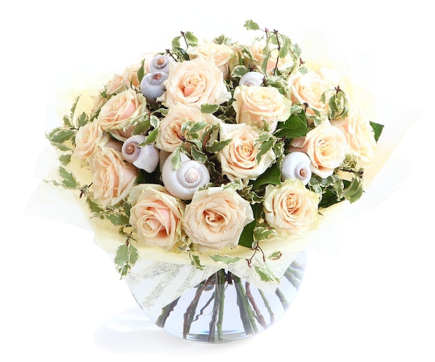 Arrangement floral avec des roses crème et des coquillages, un vase en verre transparent. Isolé sur fond blanc.