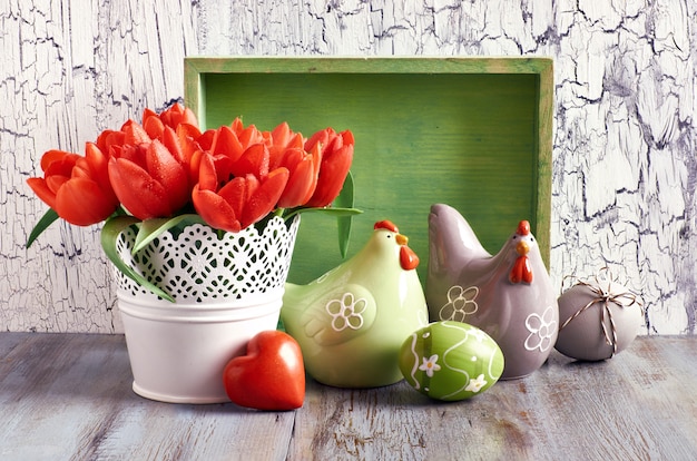 Arrangement de Pâques avec des tulipes orange, des poules en céramique et des œufs