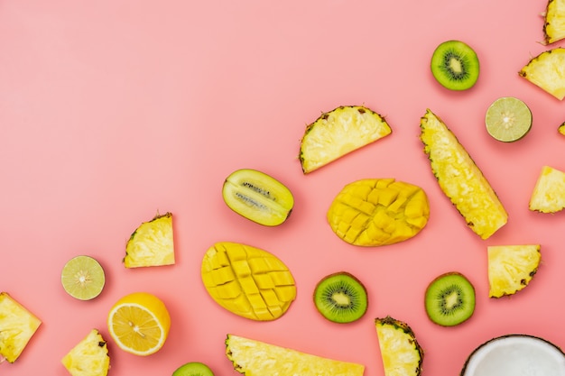 Arrangement en tranches de mangue, citron et citron vert, kiwi, ananas, sur papier rose.