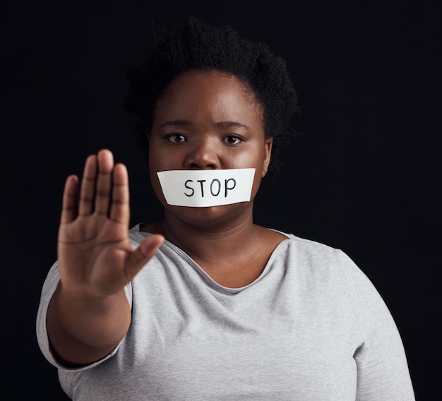 Photo arrêt de portrait et paume avec une femme noire en studio sur fond noir pour l'égalité des sexes ou la violence domestique silence ou abus de la main et une victime effrayée avec la bouche couverte de peur