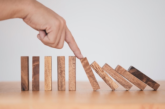 Arrêter la crise et le concept de gestion des risques, l'homme à l'aide du doigt pour arrêter le domino en bois qui tombe à un bloc de bois toujours debout.