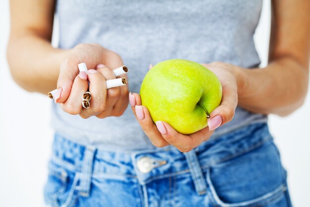 Arrêter de fumer, gros plan d'une femme tenant des cigarettes cassées et des pommes vertes