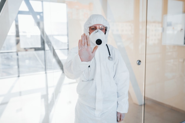 Arrêtez le geste du virus. Femme médecin scientifique en blouse de laboratoire, lunettes défensives et masque debout à l'intérieur