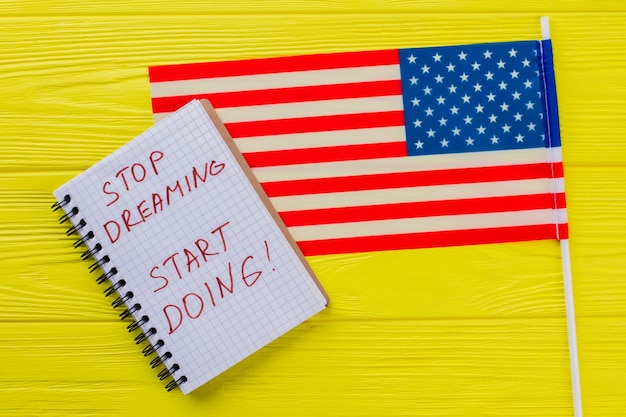 Arrêtez de rêver, commencez à faire. Slogan de motivation écrit sur le bloc-notes avec le drapeau des États-Unis sur une table en bois jaune.