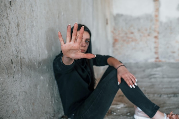 Arrêtez la violence Jeune femme battue en vêtements noirs assise sur le sol d'un bâtiment abandonné