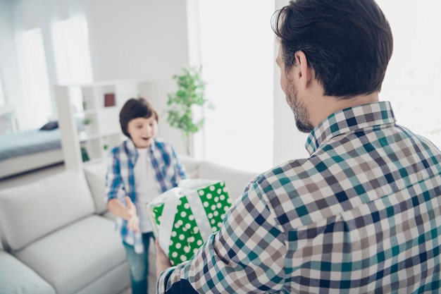 Arrière arrière derrière vue portrait de deux beaux gars joyeux joyeux heureux papa papa donnant boîte d'achat cadeau à un événement de fils pré-adolescent dans la maison intérieure moderne blanc clair salon à l'intérieur