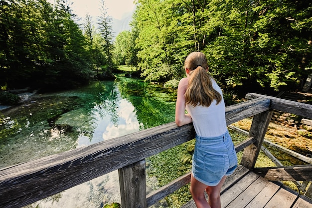 L'arrière du stand de fille dans le pont en bois de la rivière d'eau vert émeraude Sava Bohinjka dans les Alpes Juliennes Ukanc Slovénie