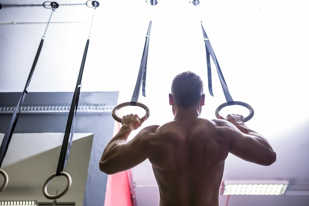 Photo arrière de l'homme musclé faisant de la gymnastique anneau